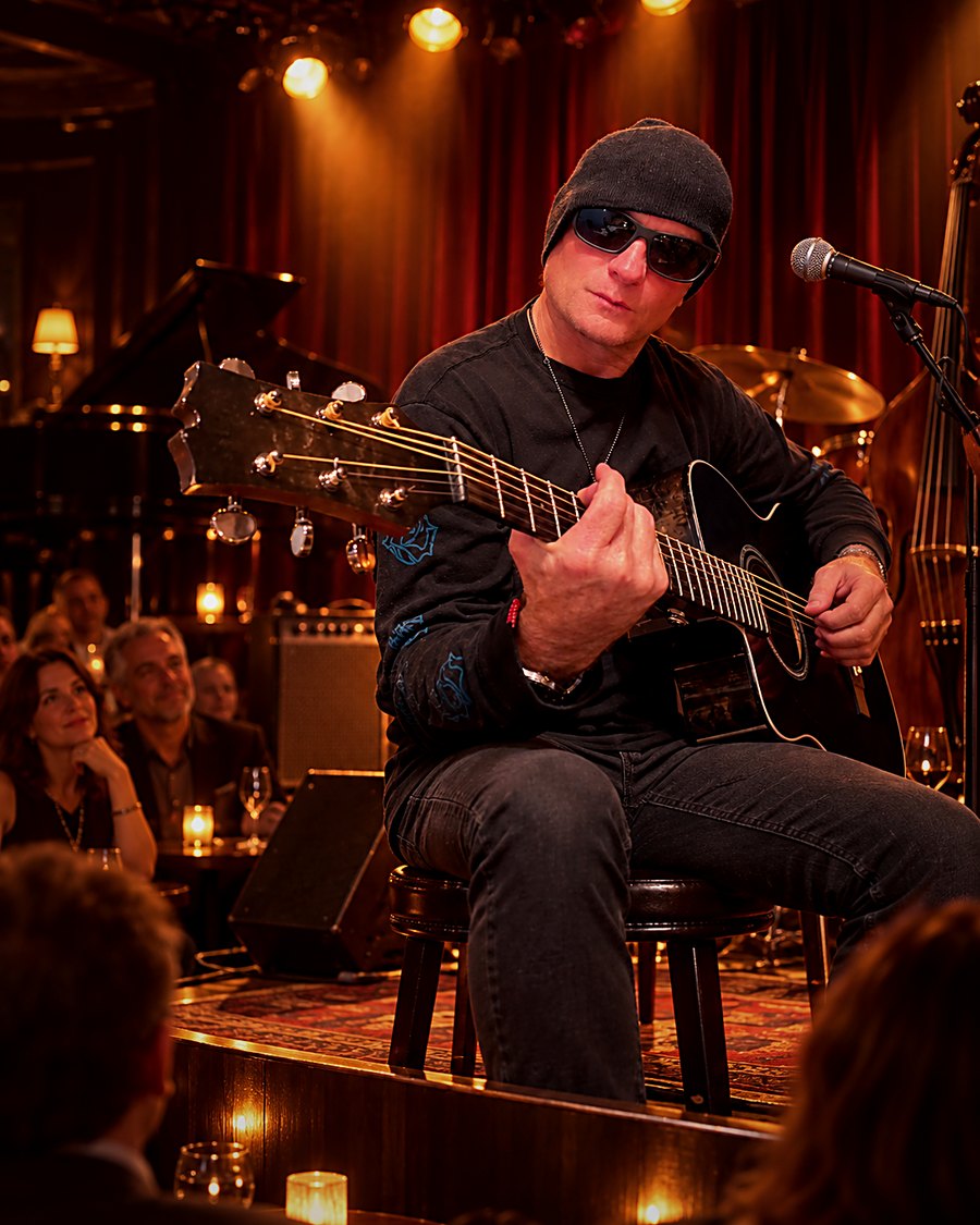Ronn Vanderhoff playing an acoustic guitar on stage in a warmly lit club